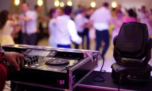 DJ miksujący muzykę na studniówce, w tle tańczący ludzie.