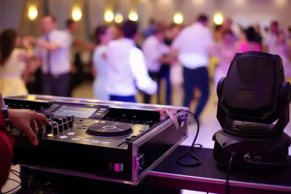 DJ miksujący muzykę na studniówce, w tle tańczący ludzie.